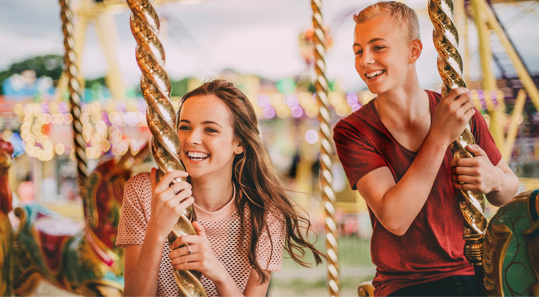 Two teenagers, smiling, riding a carousel. The phrase 'You learn, we care' is written over the image, visually interacting with them.